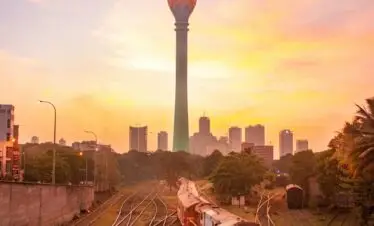Sunset view of Colombo Lotus Tower with a train on a railway track, capturing urban Sri Lankan landscape.