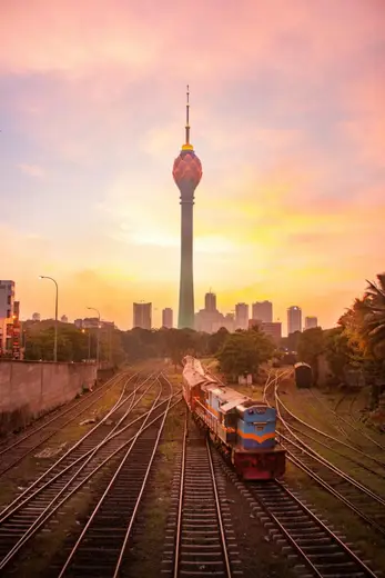 Sunset view of Colombo Lotus Tower with a train on a railway track, capturing urban Sri Lankan landscape.