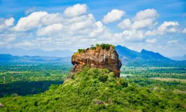 Explore the iconic Sigiriya Lion Rock surrounded by lush greenery and vibrant blue skies in Sri Lanka.