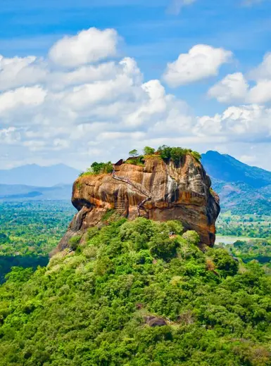Explore the iconic Sigiriya Lion Rock surrounded by lush greenery and vibrant blue skies in Sri Lanka.