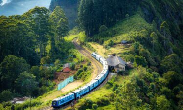 Aerial view of a picturesque train winding through lush green hills and rural houses.