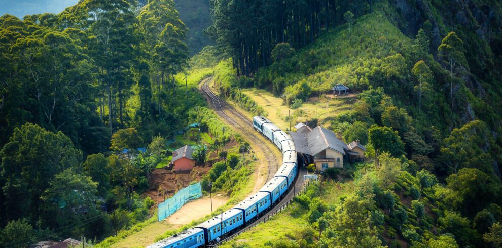 Aerial view of a picturesque train winding through lush green hills and rural houses.